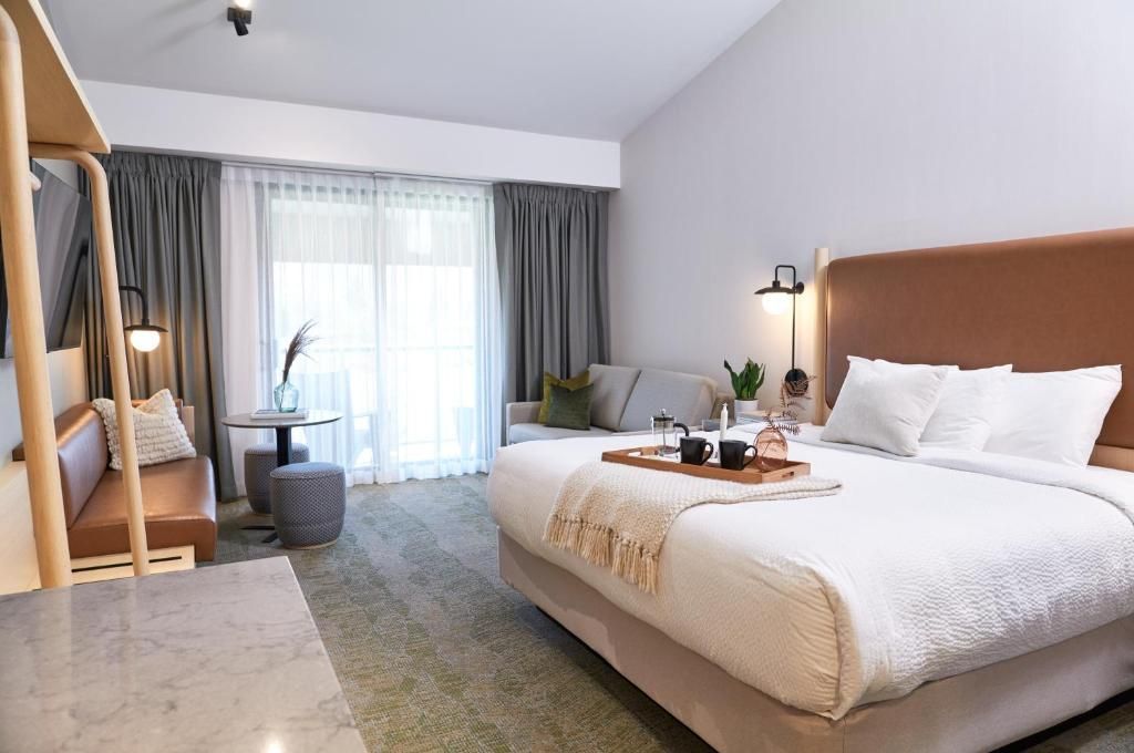 Lichte slaapkamer met kingsize bed, houten hoofdeinde, raam met gordijnen en een gezellige zithoek van Forest Park Hotel, Jasper