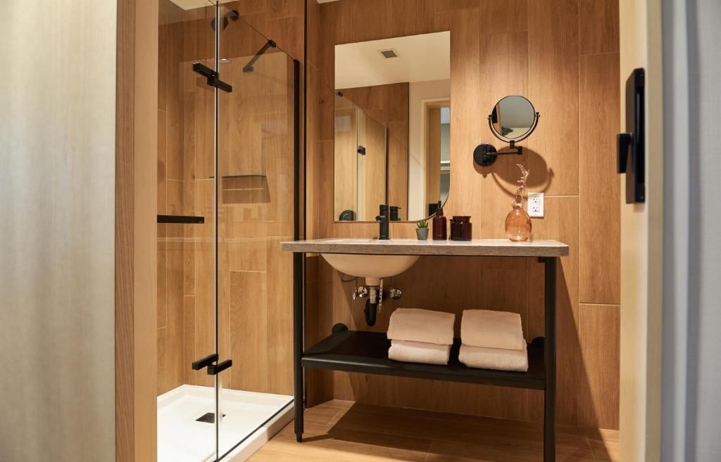 Moderne badkamer met glazen douchecabine, houten lambrisering, wastafel, spiegel en netjes opgestapelde handdoeken op een plank bij Forest Park Hotel, Jasper