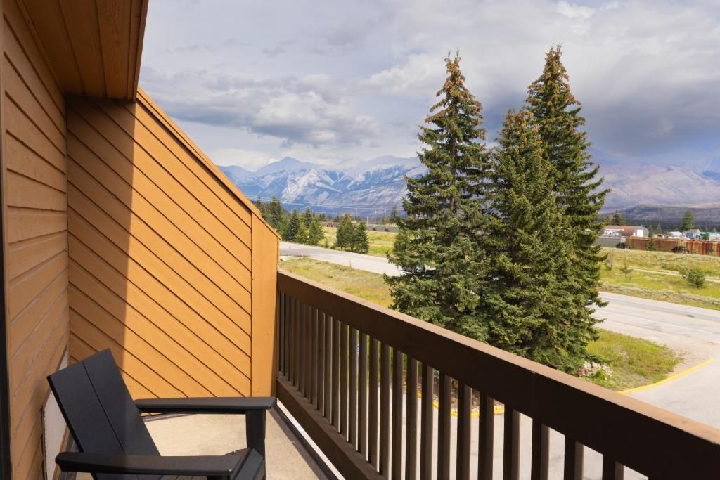 Balkon van Forest Park Hotel, Jasper met stoel, uitzicht op een weg, dennenbomen en in de verte bergen onder een bewolkte hemel.