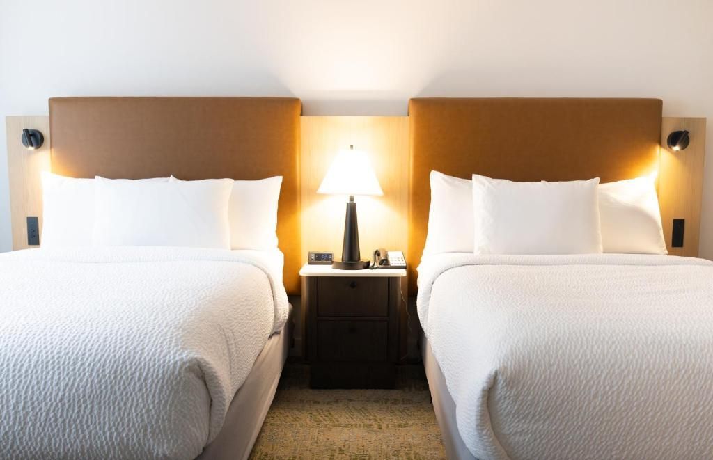 Twee witte bedden met bruine hoofdborden en een brandende lamp ertussen in een hotelkamer van Forest Park Hotel, Jasper.