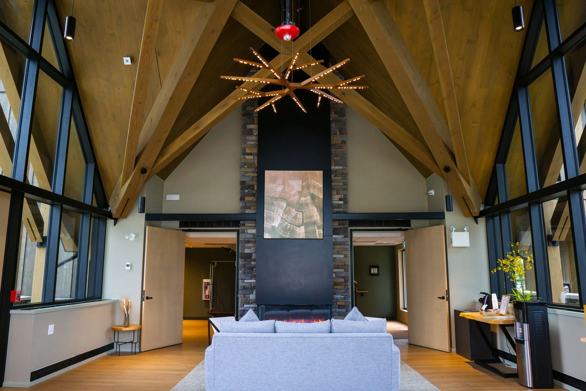 Moderne lobby van Forest Park Hotel Jasper met hoge houten balken, grote ramen, kroonluchter en een centrale zwarte open haard of pilaar.