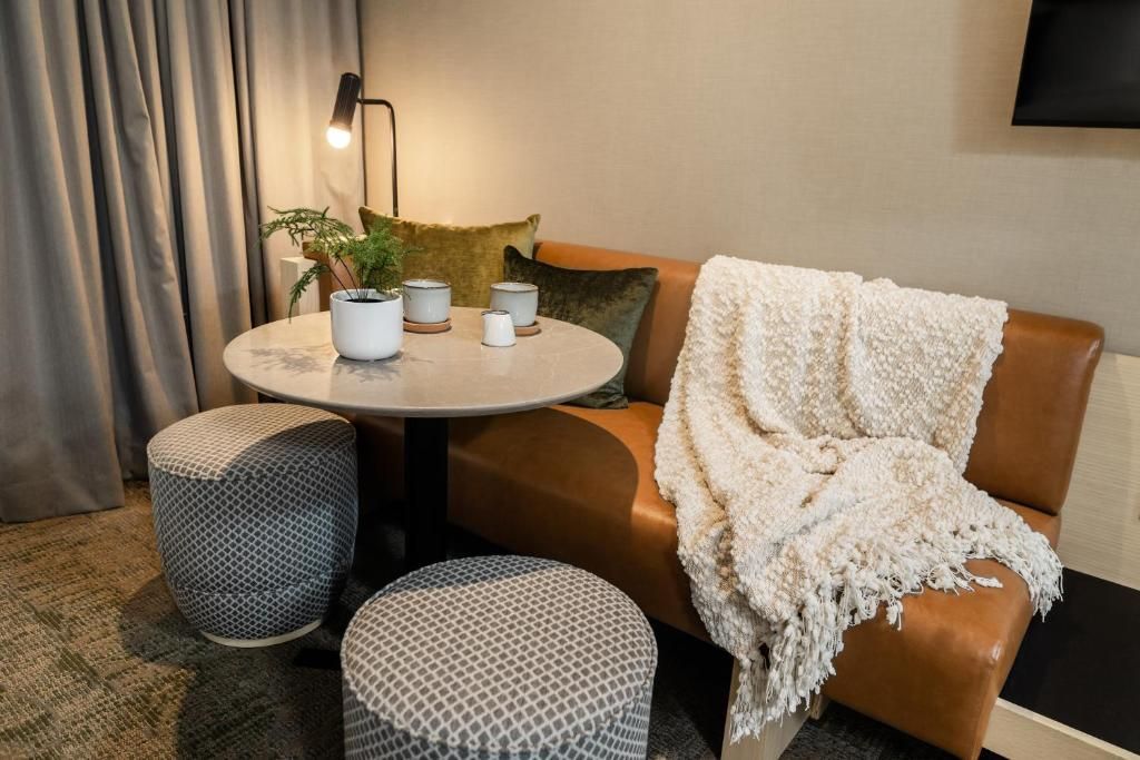Gezellige zithoek met een beige stoel, ronde tafel, gevlochten poefjes, planten en een witte plaid in een kamer van Forest Park Hotel, Jasper