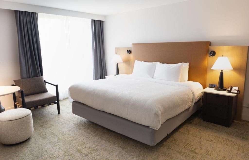 Moderne hotelkamer van Forest Park Hotel, Jasper met een groot bed, fauteuil, voetenbank, nachtlampje en een licht raam met gordijnen.