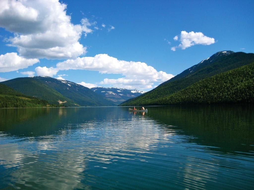 Bergmeer met kalm blauw water, beboste hellingen en wolken die in het oppervlak weerspiegelen