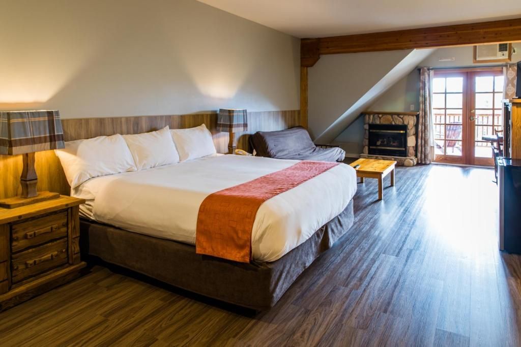 Gezellige hotelkamer met kingsize bed, houten vloer, lamp, open haard en uitzicht vanaf het balkon.