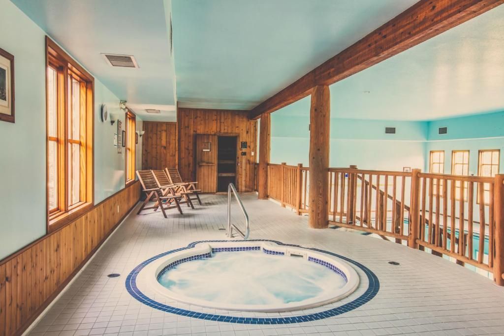 Overdekt zwembadgedeelte met een kleine ronde jacuzzi, houten balustrade, ligstoelen en grote ramen.
