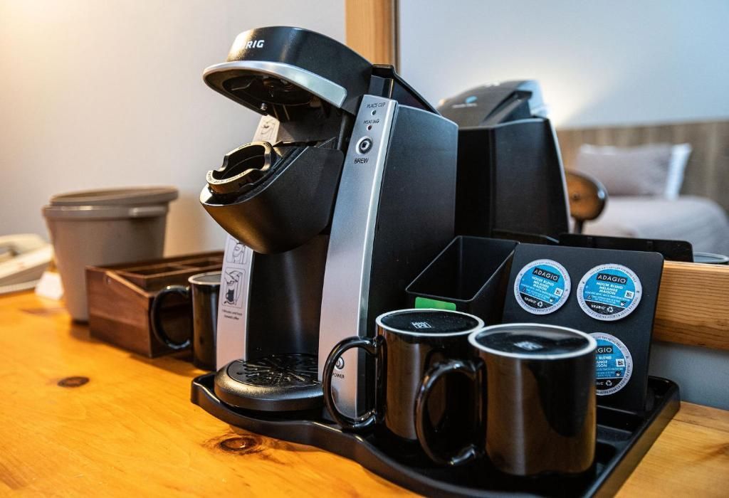 Een koffiezetapparaat met twee zwarte mokken en een bakje koffiepads op een houten tafel.