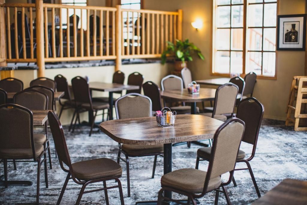 Gezellige zithoek in caféstijl met houten tafels, comfortabele stoelen, grote ramen en warme verlichting.