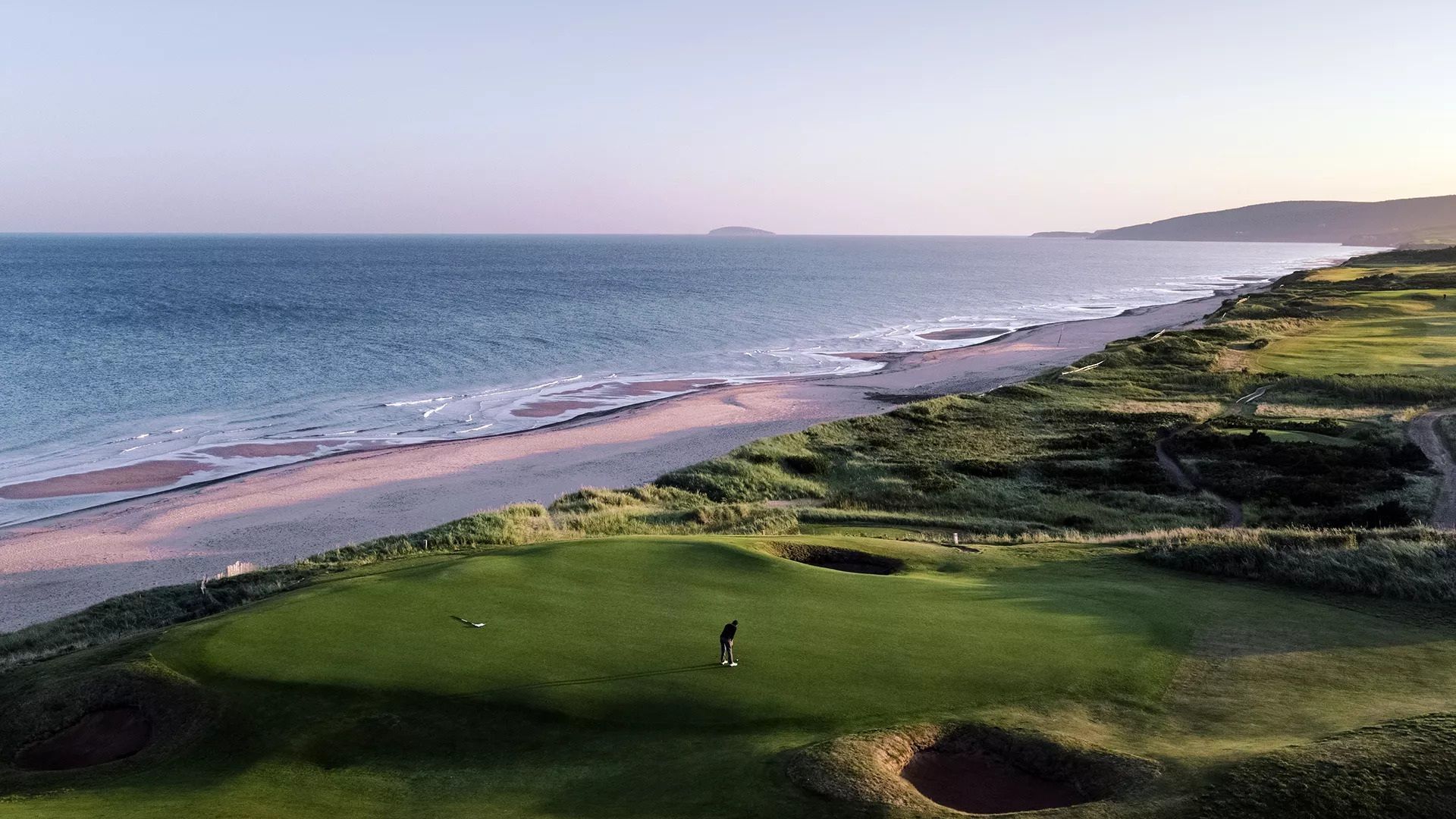 Golfbaan aan de kust, naast een zandstrand en de blauwe oceaan bij zonsondergang.