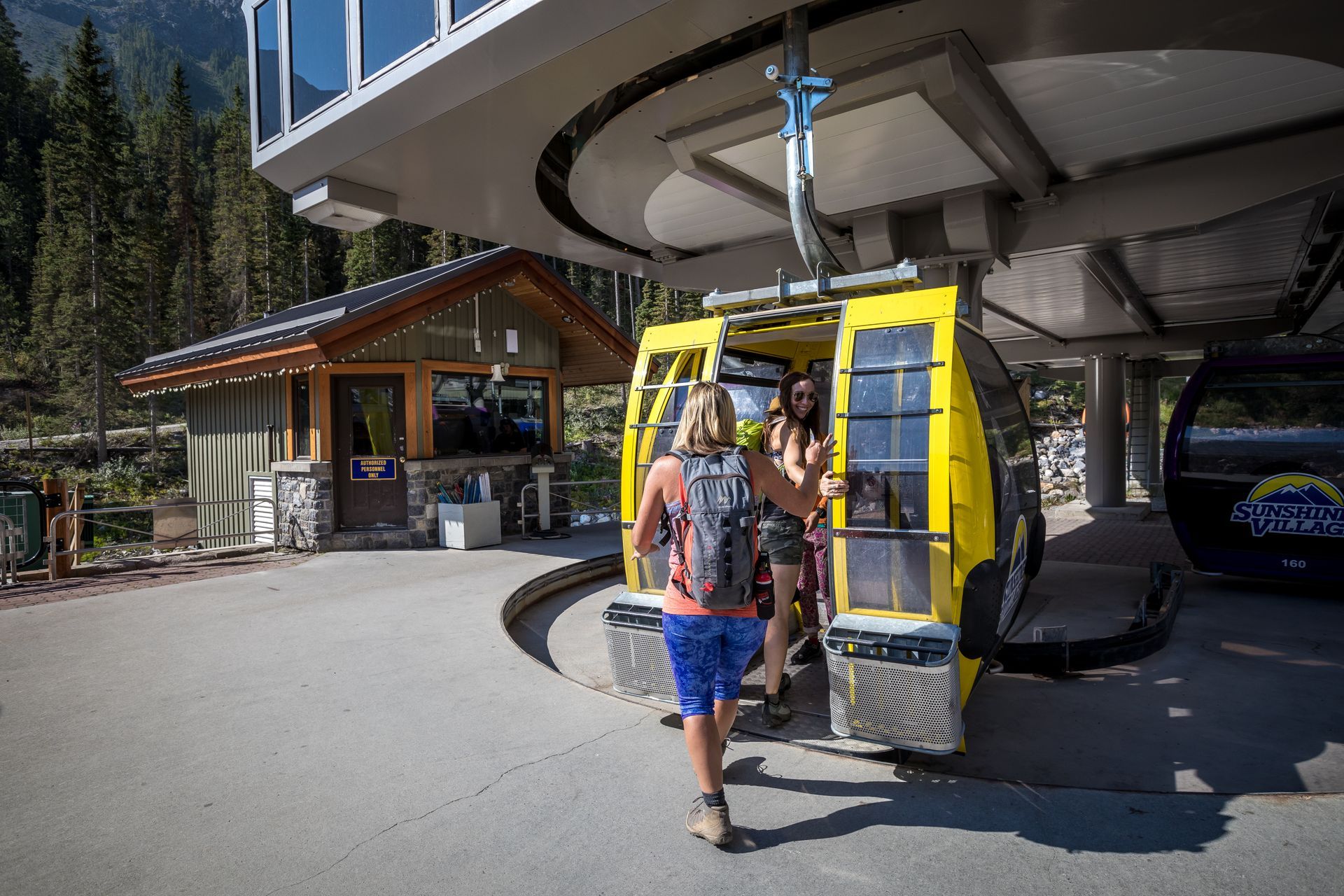 Twee mensen stappen in een gele gondel bij een kabelbaanstation in de bergen van Banff.