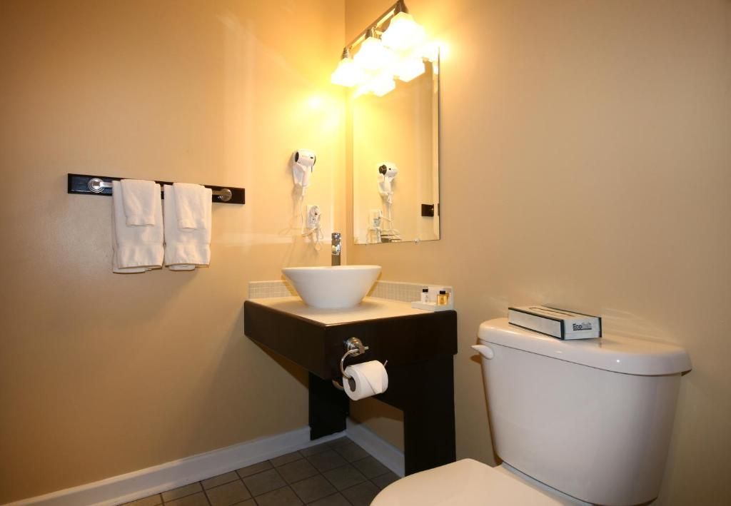Kleine beige badkamer met wastafel op een voetstuk, spiegel, handdoekrek en toilet.