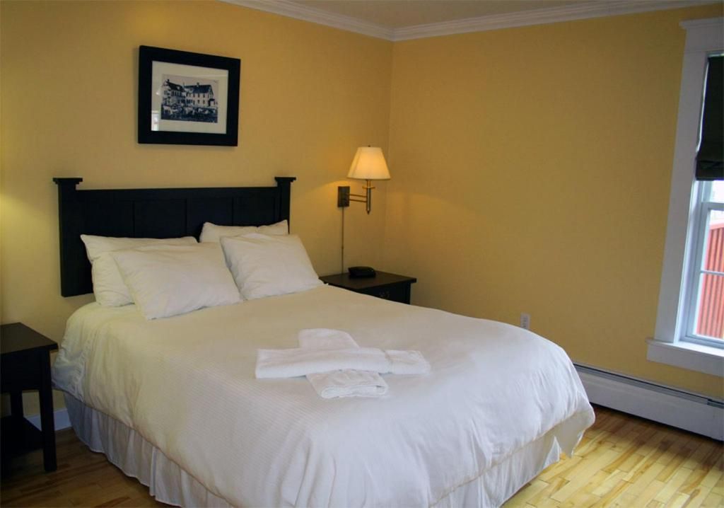 Een net opgemaakt bed in een gele slaapkamer met nachtlampjes en ingelijste kunstwerken aan de muur.