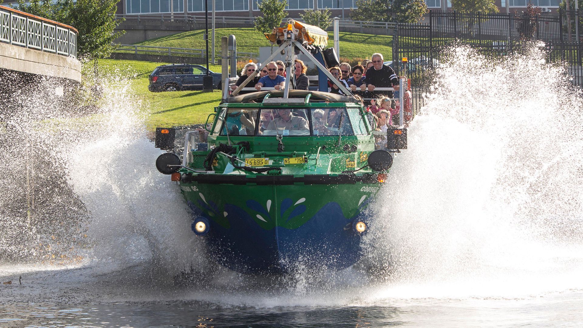 Een groene rondvaartboot raast door het water en spat aan beide kanten hoog op.