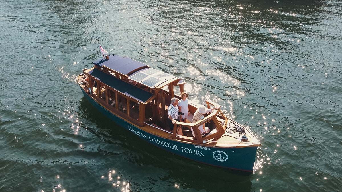 Een houten rondvaartboot vaart over het glinsterende water, met passagiers op het dek en in een overdekte cabine.