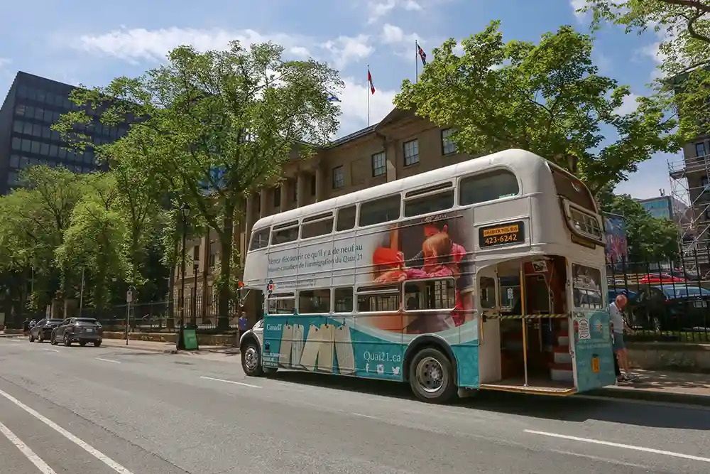 Een open touringcar rijdt door een met bomen omzoomde stadsstraat.