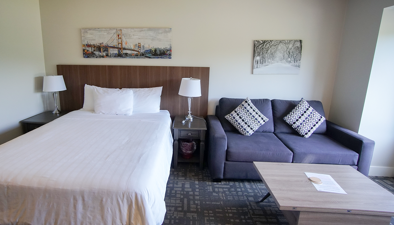 Slaapkamer met een wit bed, een grijze bank en twee kunstwerken aan de muur in een moderne hotelkamer.