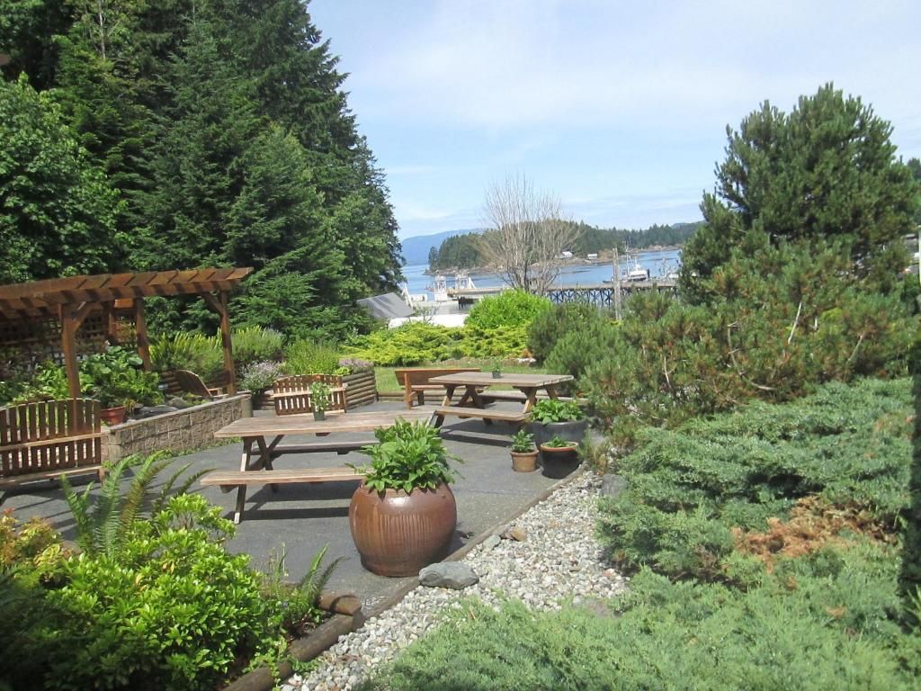 Tuinpatio met picknicktafels, potplanten en uitzicht op het water in de verte.