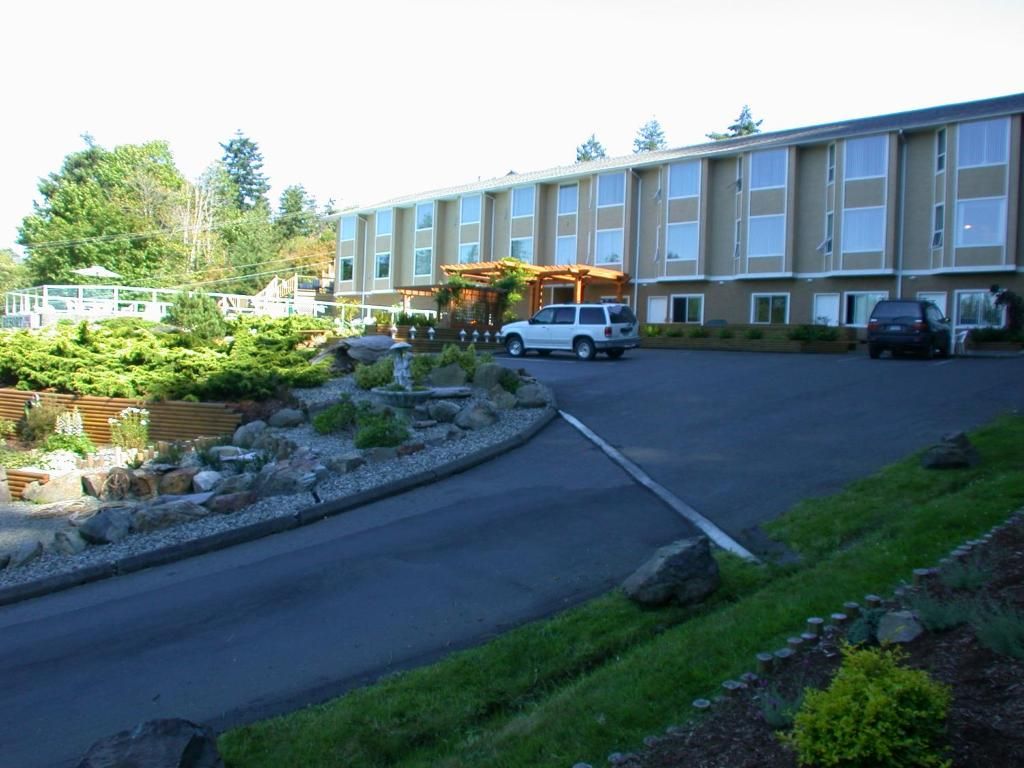 De buitenkant van een motel met een gebogen oprit, geparkeerde auto's en een aangelegde rotstuin in de schemering.