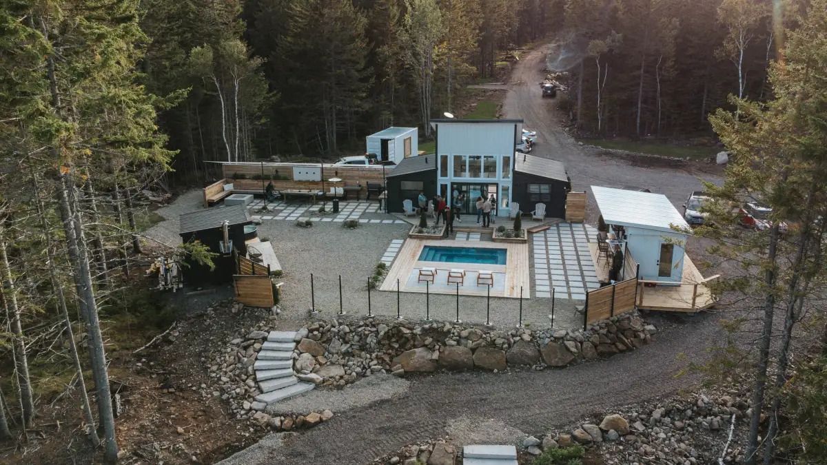 Luchtfoto van een modern huis met een terras en zwembad, omgeven door bomen en een kronkelende onverharde oprit.