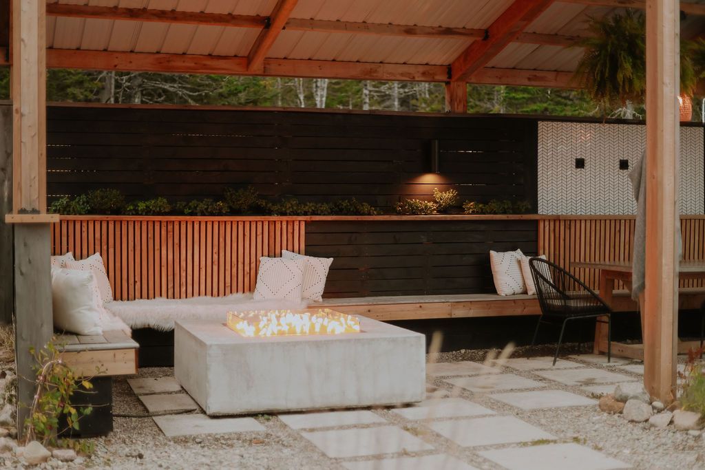 Overdekte buitenlounge met witte kussens, houten banken en een stenen terras onder een rood dak.
