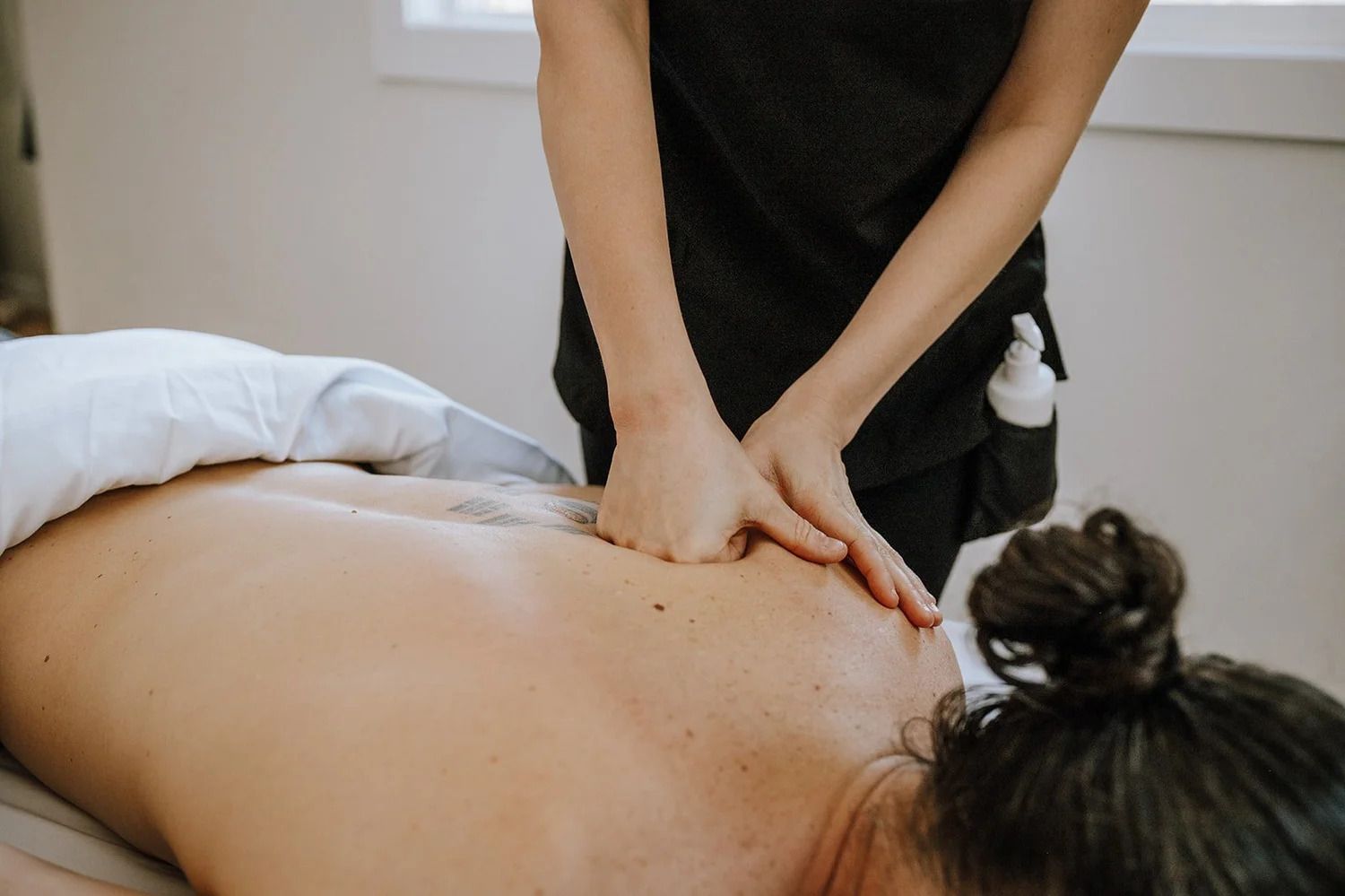 Een massagetherapeut geeft een rugmassage aan een cliënt die op een massagetafel ligt.