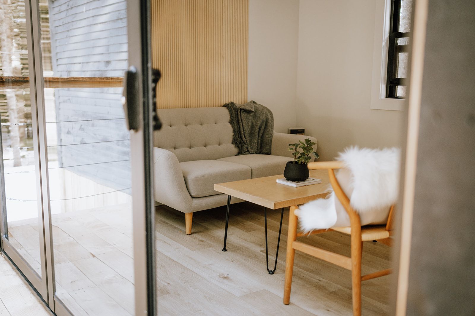 Gezellige, moderne woonkamer met beige bank, houten stoel, salontafel en zachte witte decoratie.