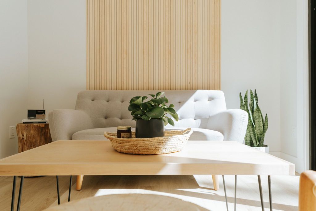 Lichte, minimalistische woonkamer met beige bank, houten salontafel en potplanten bij het raam.
