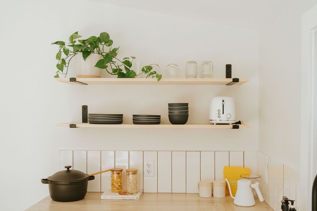 Minimalistische keukenplank met planten, servies, potjes en een witte waterkoker op een licht houten aanrecht.
