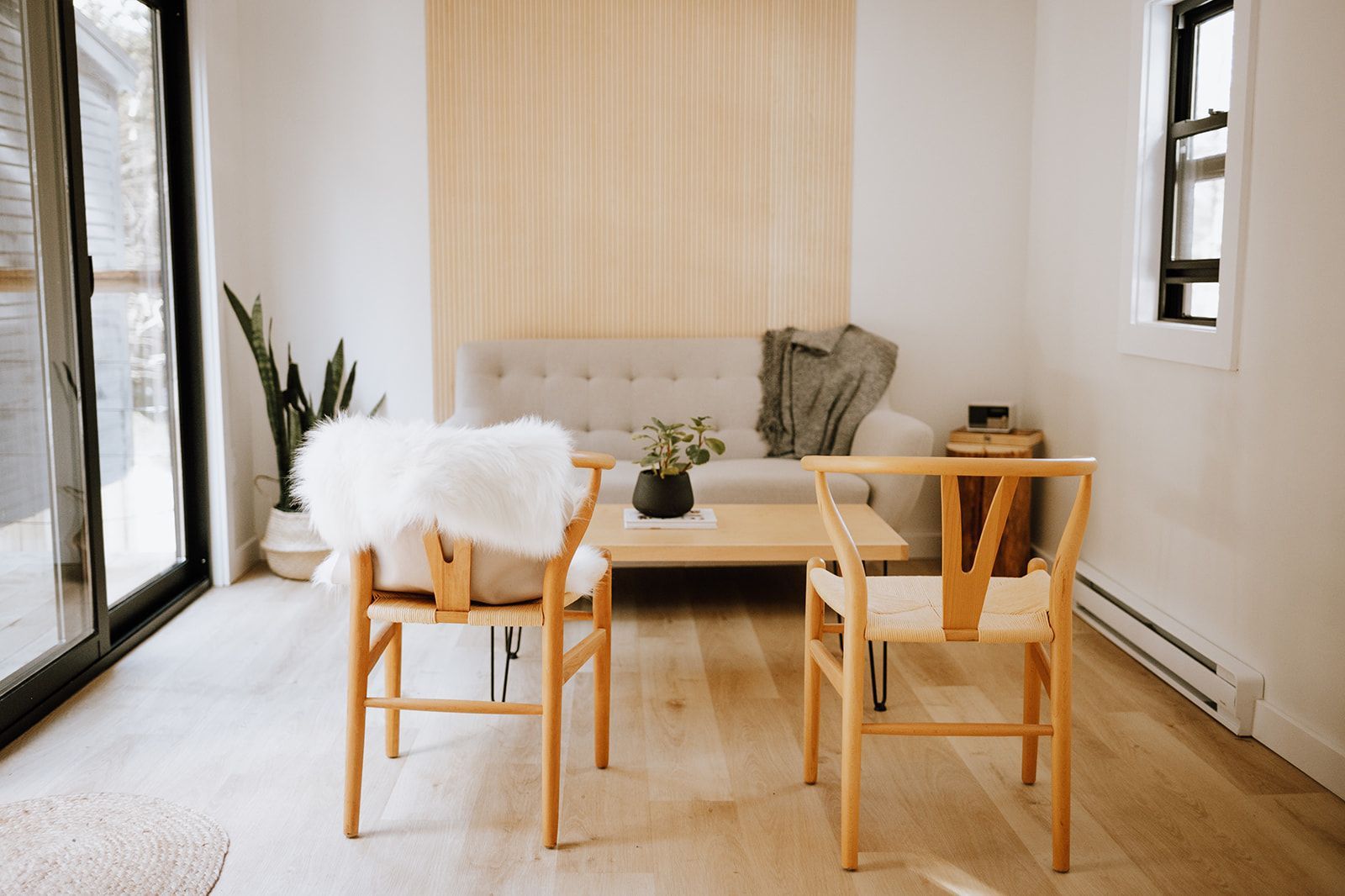 Lichte eethoek met twee houten stoelen, een lage tafel en een zachte witte plaid bij grote ramen.