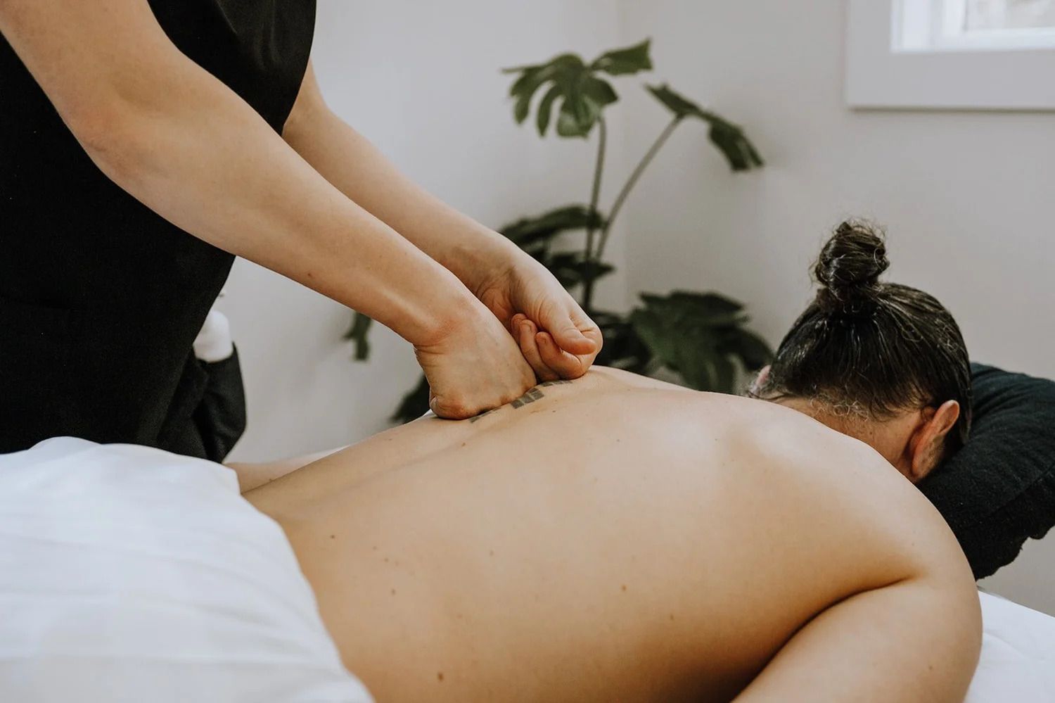 Een massagetherapeut kneedt de rug van een cliënt op een behandeltafel in een lichte sparuimte.