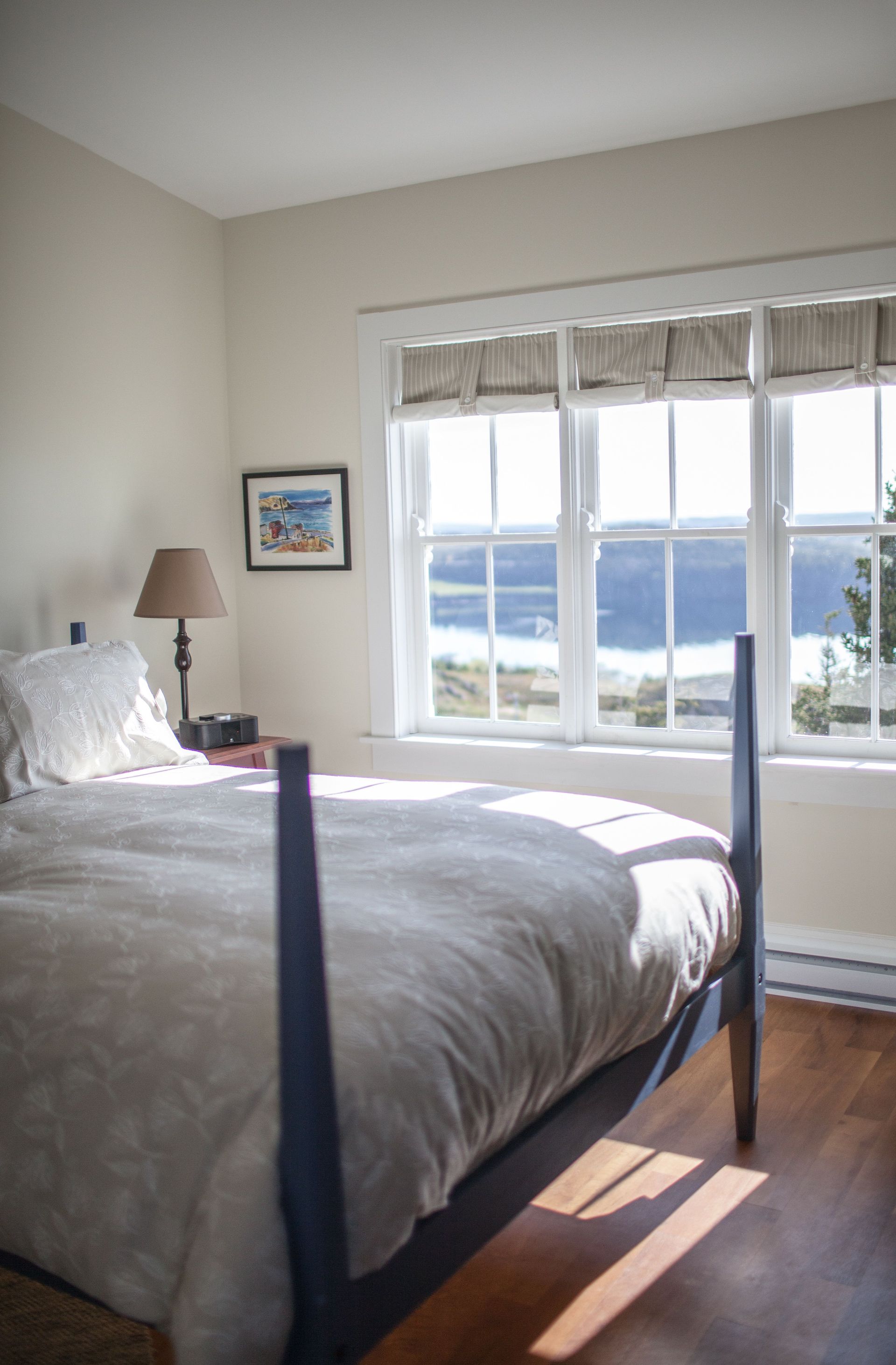 Slaapkamer van Fisher's Loft Inn in Port Rexton met bed, lamp en groot raam met uitzicht op het water.