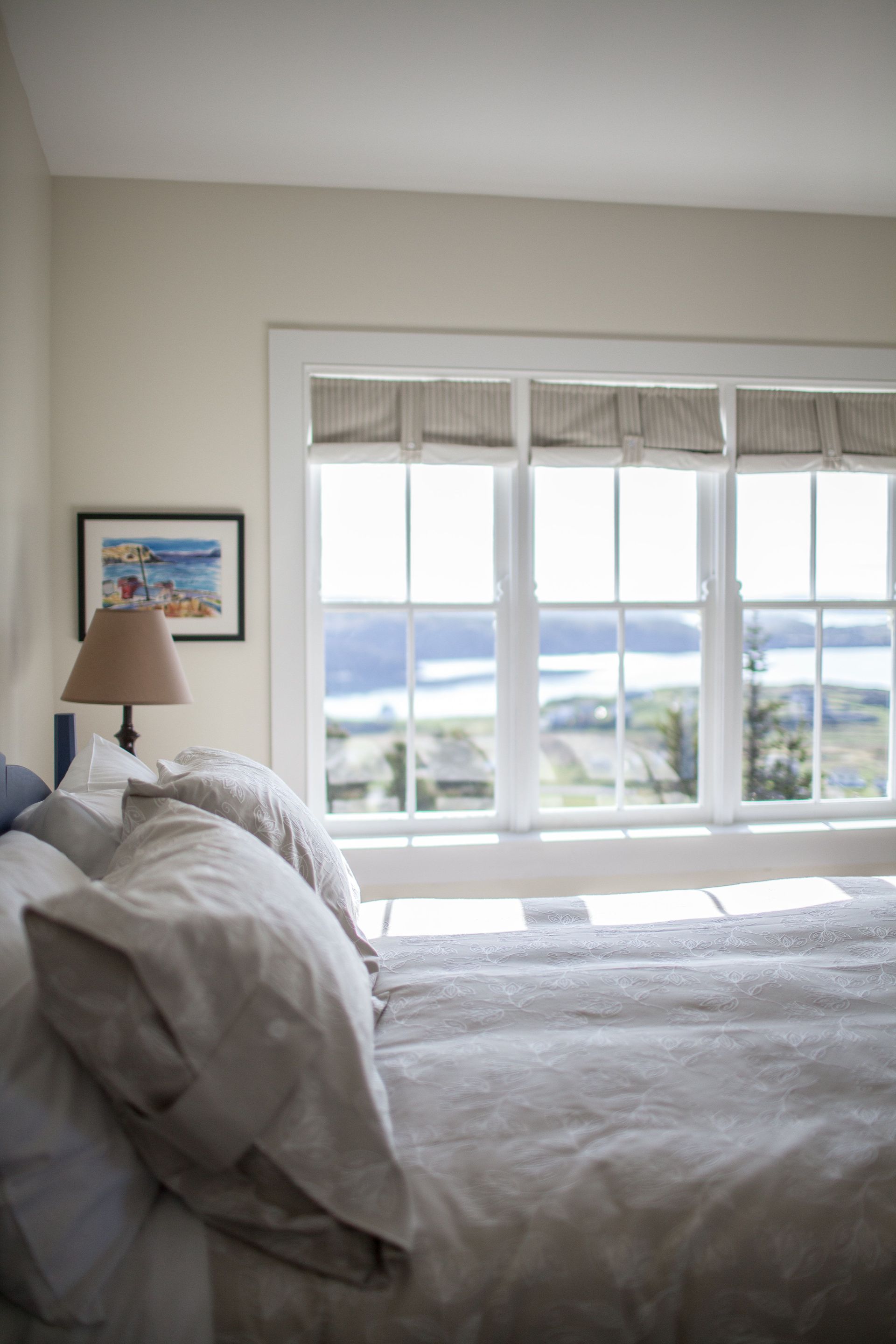 Lichte slaapkamer van Fisher's Loft Inn in Port Rexton met een opgemaakt bed, nachtlampje en een groot raam met uitzicht op de kust.