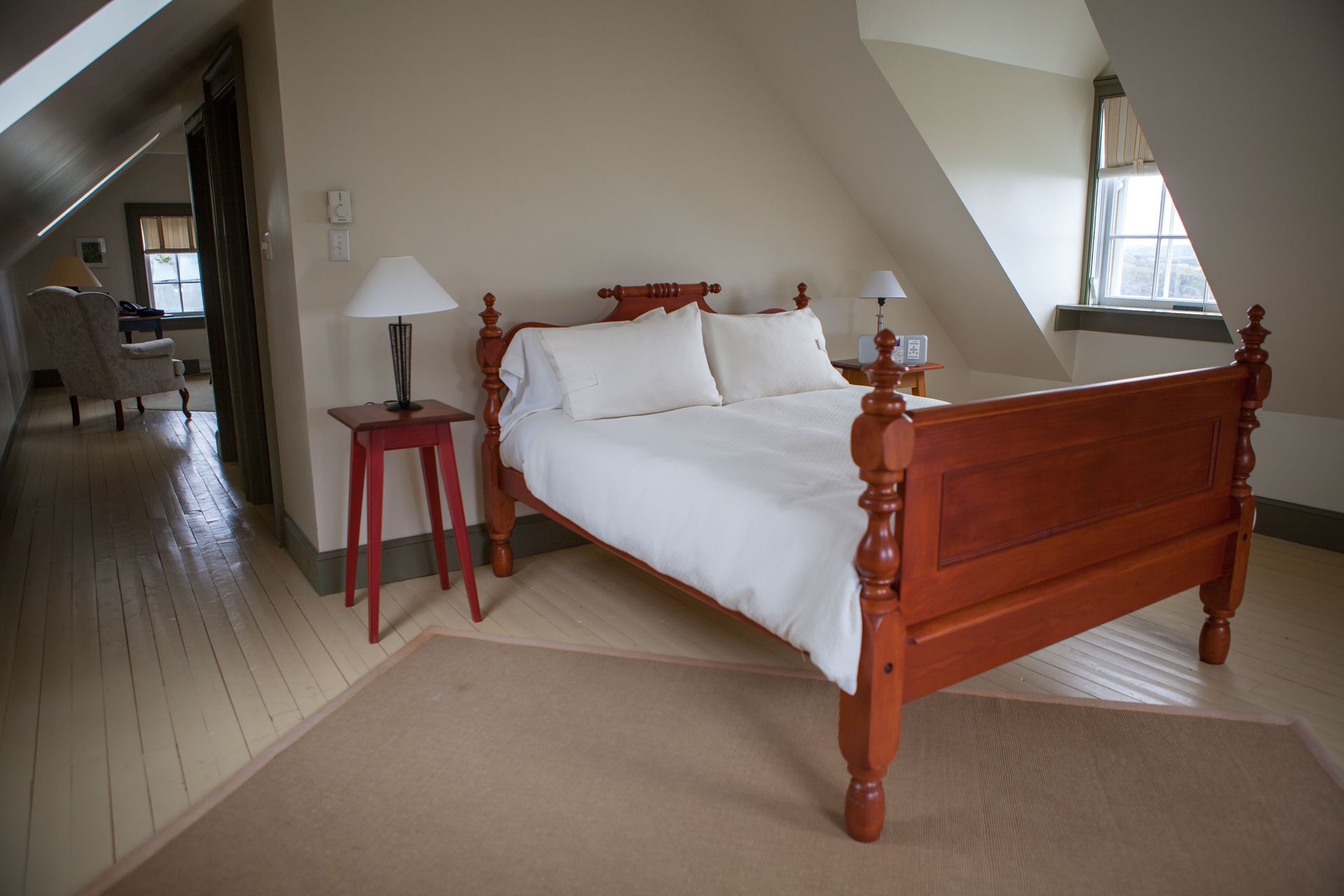 Lichte slaapkamer van Fisher's Loft Inn in Port Rexton met een houten bed, wit beddengoed en een schuin plafond, gezien vanuit de deuropening.