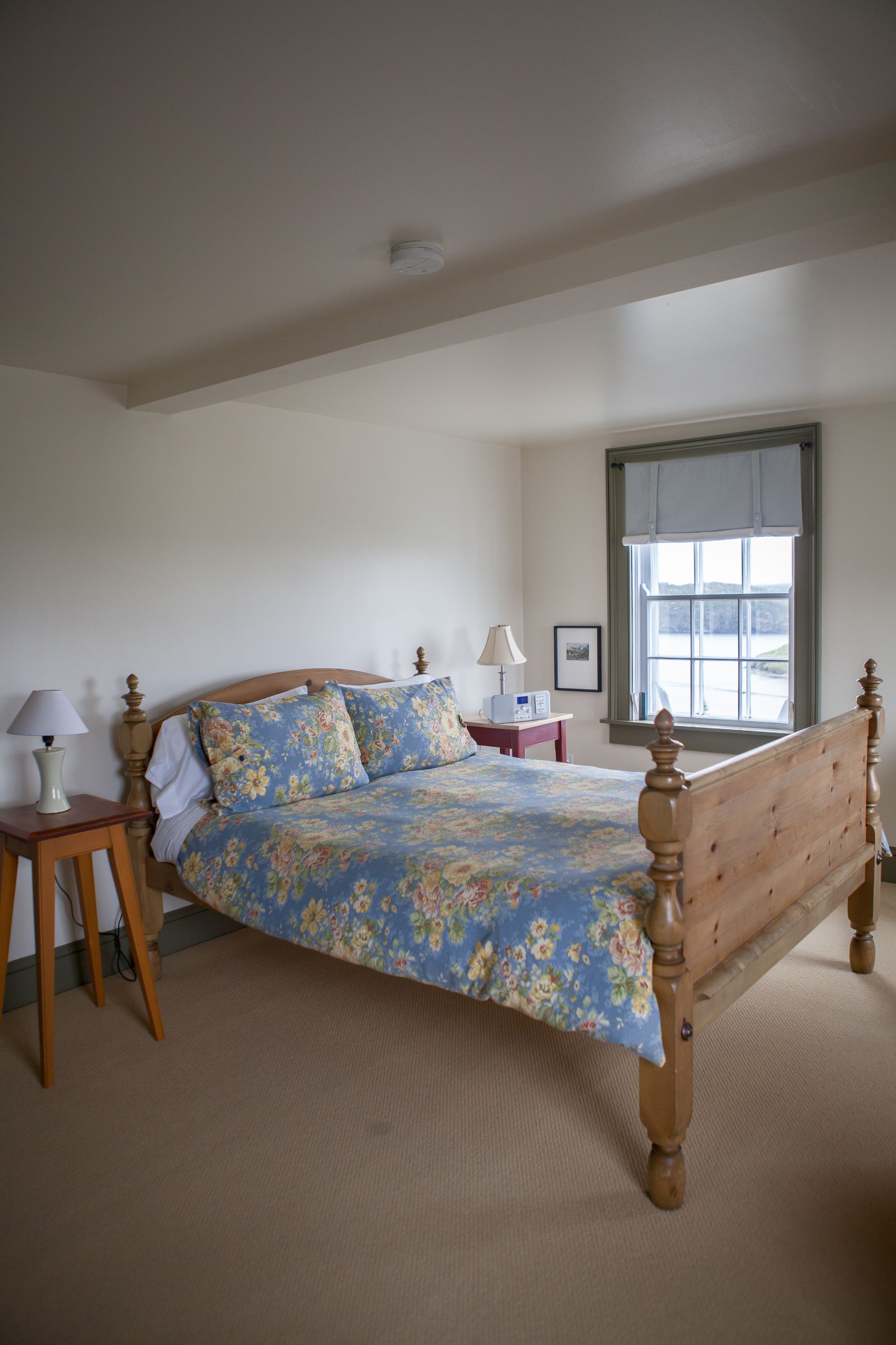 Slaapkamer van Fisher's Loft Inn in Port Rexton met een houten bed opgemaakt met blauw bloemenbeddengoed, een nachtkastje en een raam met grijze gordijnen.