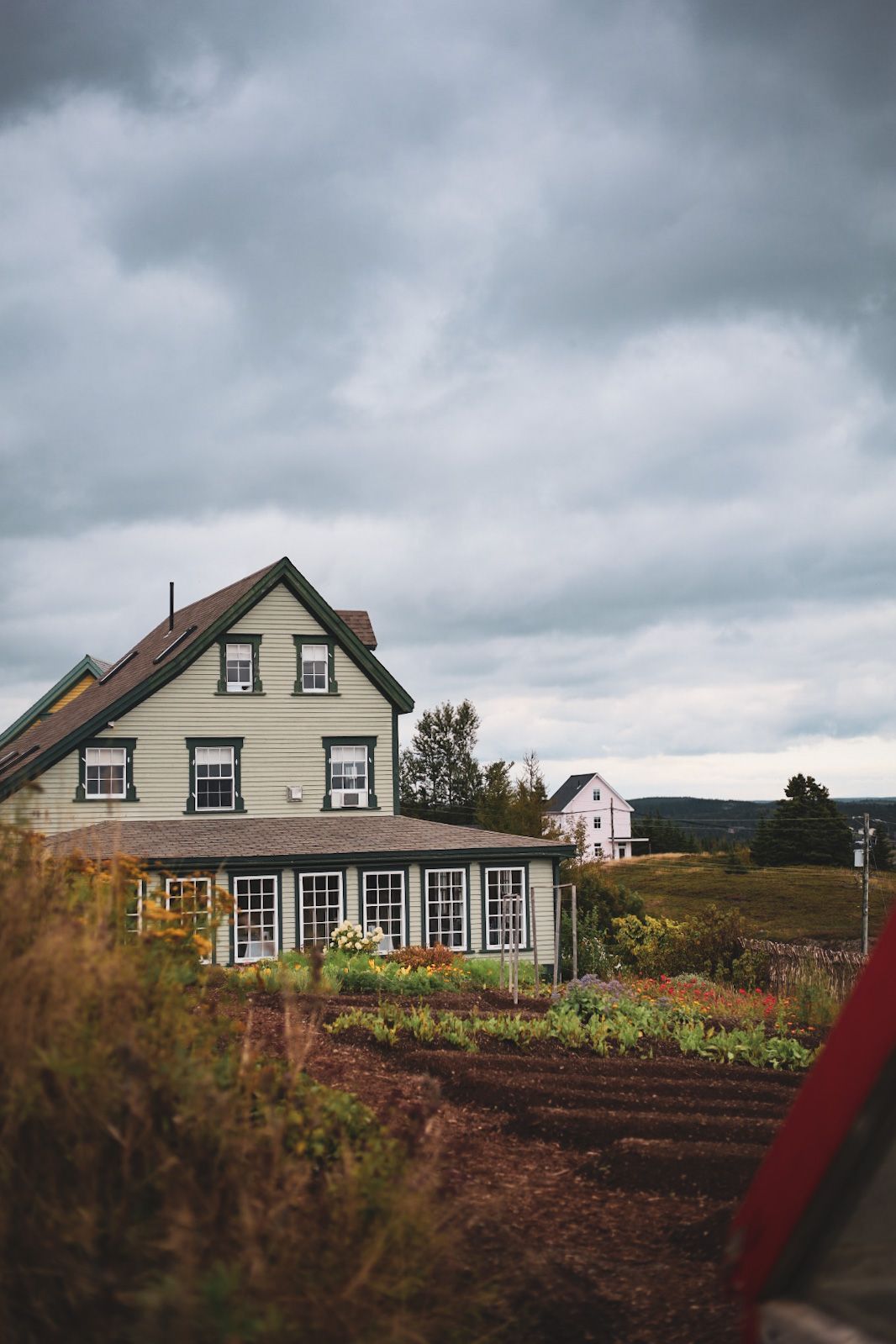 Landhuis Fisher's Loft Inn in Port Rexton met witte gevelbekleding en rood dak naast een tuin onder een bewolkte hemel.