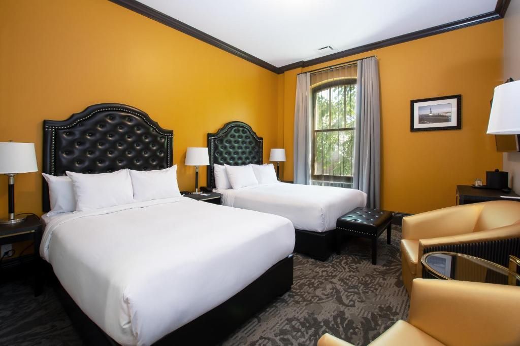 Hotelkamer met twee witte bedden, mosterdkleurige muren en een raam met gordijnen.