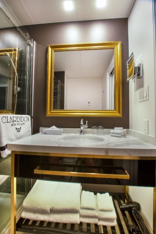 Klein hotelbadkamermeubel met spiegel met gouden lijst, marmeren wastafel en netjes opgevouwen handdoeken eronder.