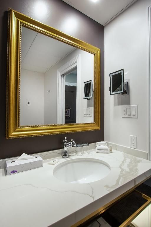 Badkamermeubel met spiegel met gouden frame, wit aanrechtblad, wastafel en aan de muur gemonteerde dispenser.