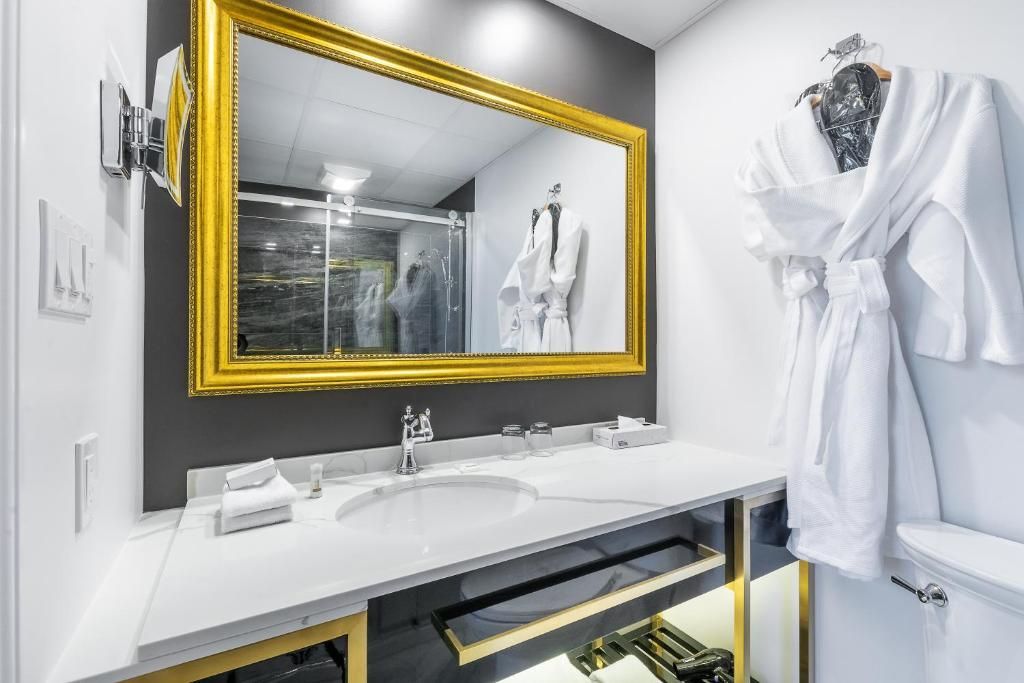 Moderne badkamer met goudkleurige spiegel, witte wastafel en witte badjas aan een haak.