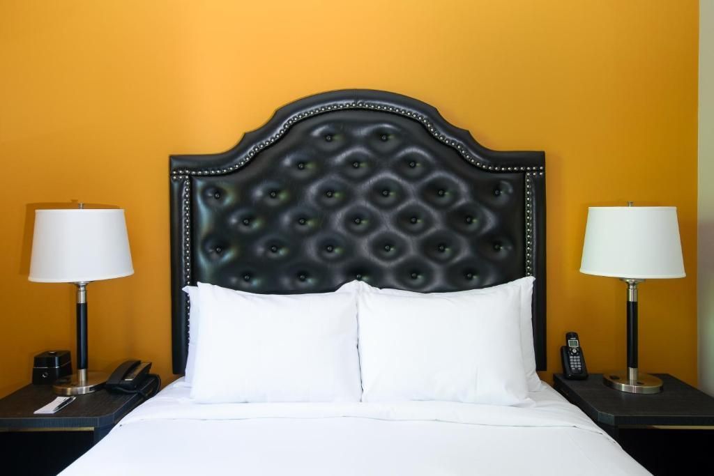 Zwart gecapitonneerd hoofdbord met witte kussens en bed tegen een mosterdgele muur, geflankeerd door twee lampen.