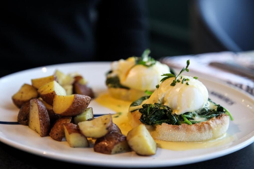 Eggs Benedict met hollandaisesaus en geroosterde aardappelen op een wit bord.