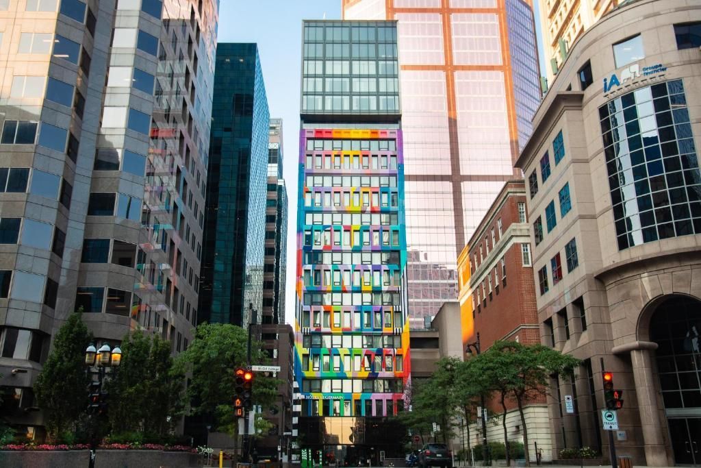 De kleurrijke glazen wolkenkrabber van Hotel Germain in het stadscentrum van Montréal, geflankeerd door hoge kantoorgebouwen en bomen.