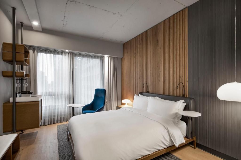 Moderne hotelkamer van Hôtel Le Germain Montréal met een groot bed, blauwe stoel, houten accentmuur en kamerhoge gordijnen.