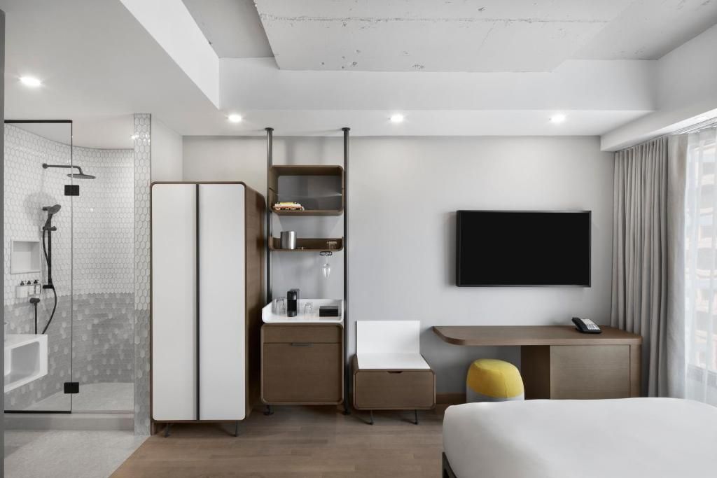 Moderne hotelkamer van Hôtel Le Germain Montréal met bed, tv, bureau, kledingkast, planken en balkondeuren.