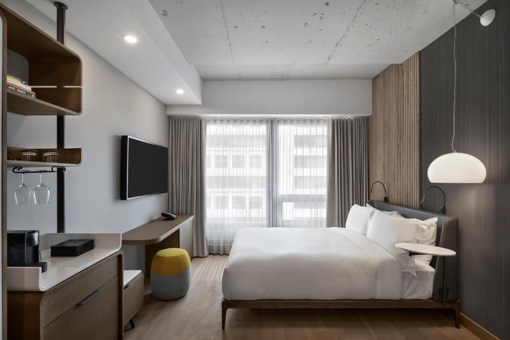 Moderne hotelkamer van Hôtel Le Germain Montréal met kingsize bed, aan de muur gemonteerde tv, bureau en ramen van vloer tot plafond.