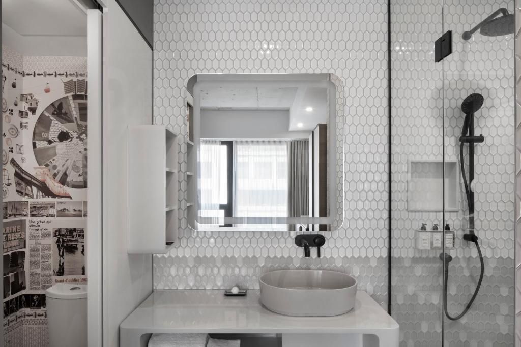 Moderne witte badkamer van Hôtel Le Germain Montréal met zeshoekige tegelwanden, ronde wastafel, spiegel en zwarte douchekranen.