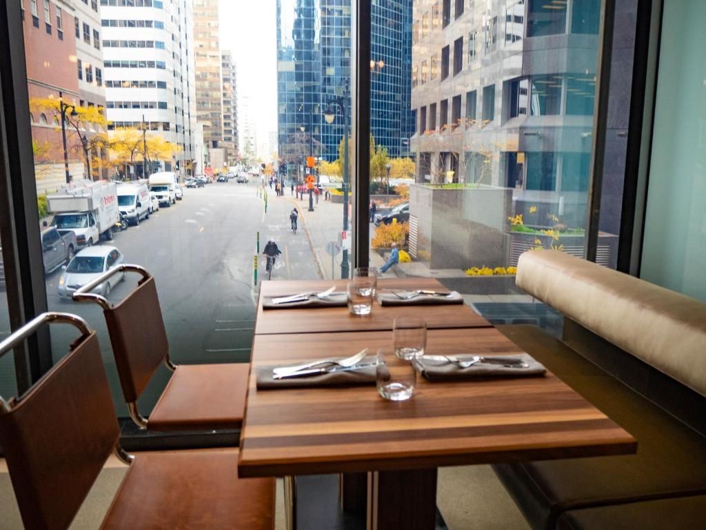 Restaurantzitje van Hôtel Le Germain Montréal naast grote ramen met uitzicht op een stadsstraat en hoge gebouwen.
