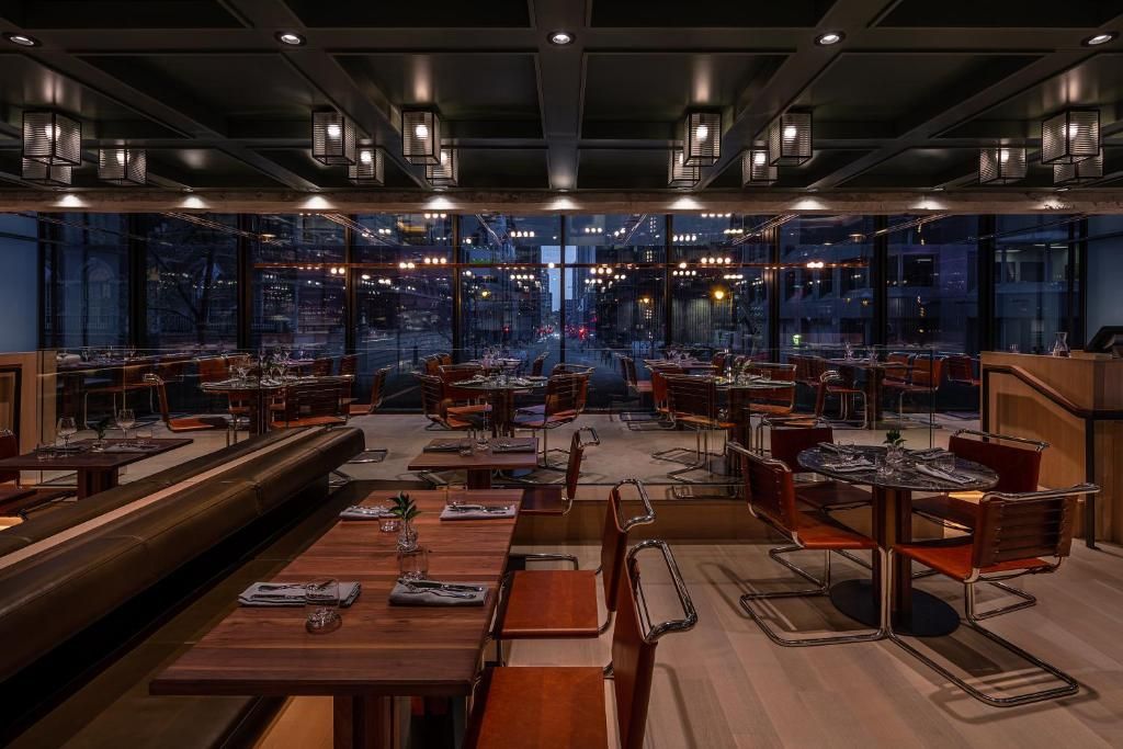 Modern, chique restaurant van Hôtel Le Germain Montréal met rode stoelen, lange tafels en uitzicht op de stadslichten door grote ramen.