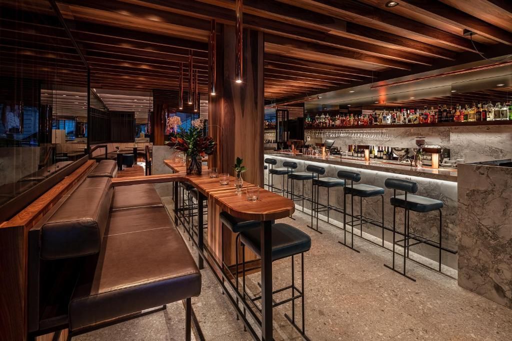 De sfeervolle, moderne bar van Hôtel Le Germain Montréal met houten tafels, leren banken en een lange bar met barkrukken.