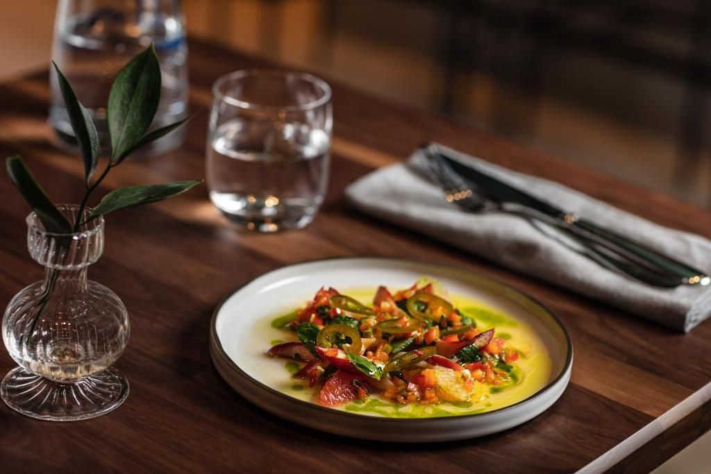 Een fraai opgemaakt gerecht op een houten tafel van Hôtel Le Germain Montréal, met een waterglas, servet, bestek en een klein vaasje.